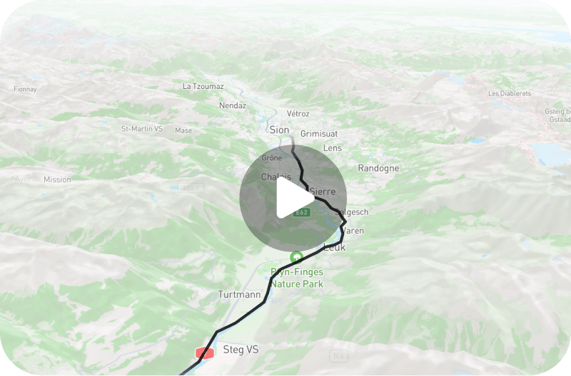 A 3D map view showing a winding route through mountainous terrain, overlaid with a dark path line that runs north–south past towns labeled Sierre, Leuk, and Steg VS. A semi-transparent circular play button sits near the center, indicating a route video. Green areas mark lowland and valleys, while pale gray and white indicate higher mountains and ridgelines. The map includes highway markers (E62) and a green nature-park pin for "Rhône-Finges Nature Park.
