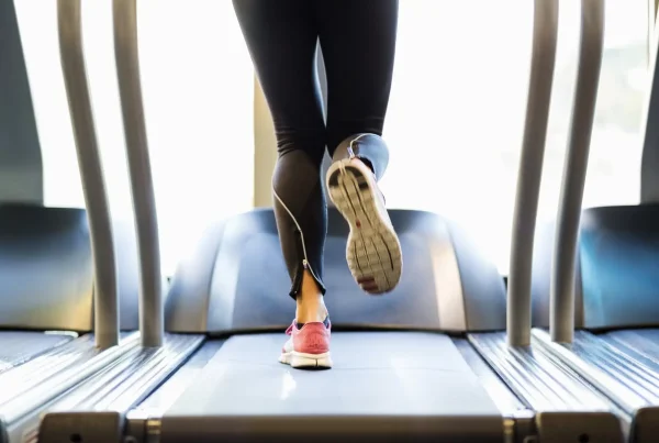 Close-up back view of a woman running on a treadmill wearing black leggings and pink sneakers, illustrating a scientific study on diet vs. exercise for weight loss
